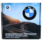 Box packaging for BMW floating center caps, featuring the BMW logo, a winding mountain road photo, and German and English text reading 'FLOATING CENTER CAPS' and 'ORIGINAL BMW ACCESSORIES.'.