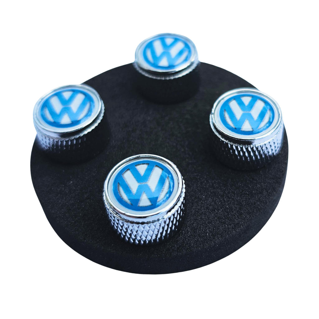 Four VW Volkswagen logo tire valve caps on a black background out of packet