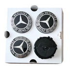 Four Mercedes-Benz floating dynamic wheel centre caps mounted on a white square backing card. 3 show the silver Mercedes star logo with black background and 'MERCEDES BENZ' text, and one shows the reverse black side of the pieces.