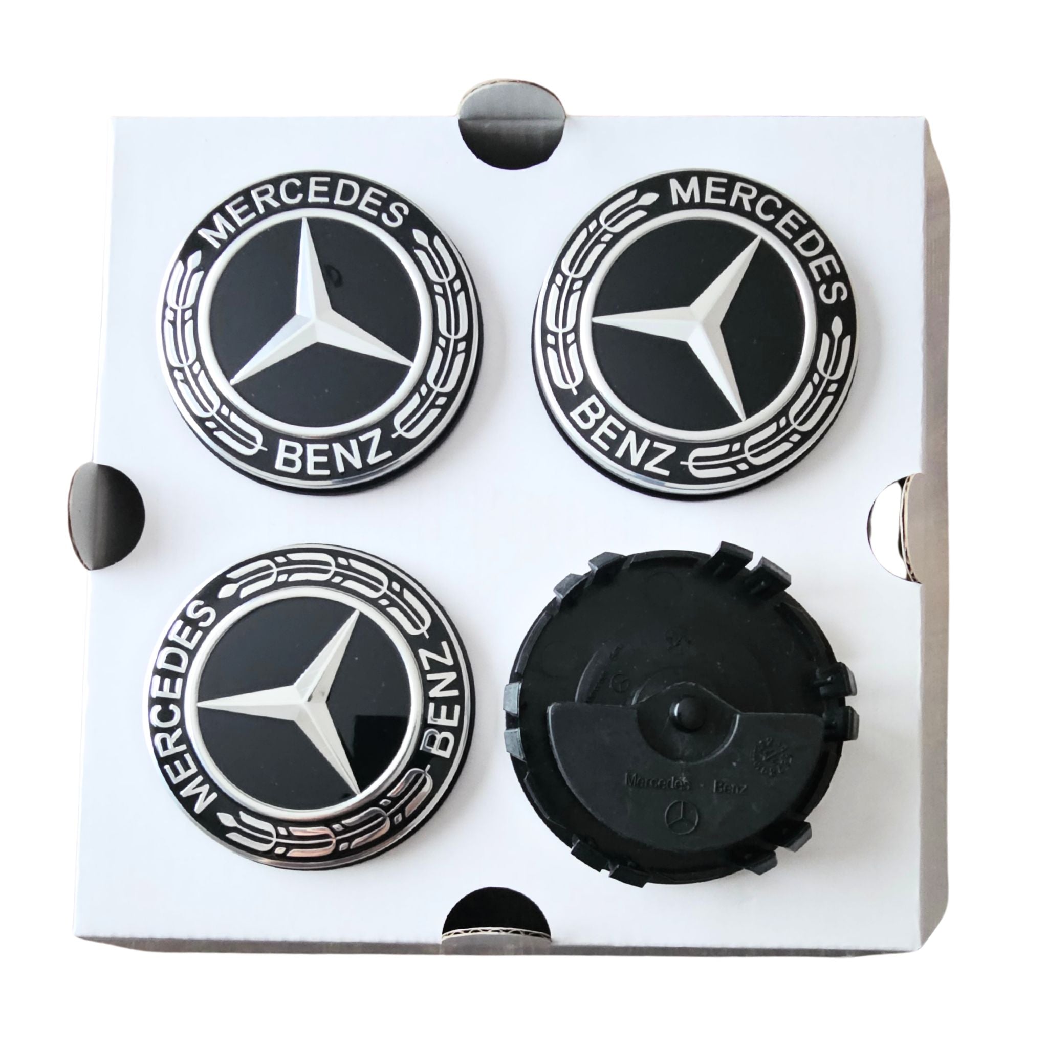 Four Mercedes-Benz floating dynamic wheel centre caps mounted on a white square backing card. 3 show the silver Mercedes star logo with black background and 'MERCEDES BENZ' text, and one shows the reverse black side of the pieces.